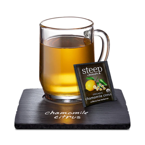 Glass mug of golden chamomile citrus tea with a Steep tea bag on a slate coaster