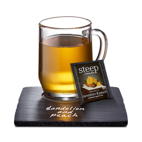 Glass mug of golden dandelion peach tea with a Steep tea bag on a slate coaster