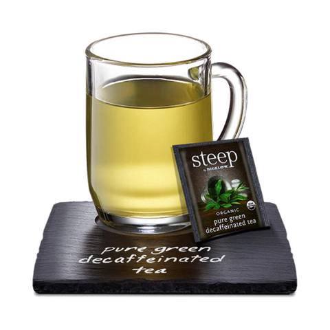 Glass mug of light green decaf green tea with a Steep tea bag on a slate coaster