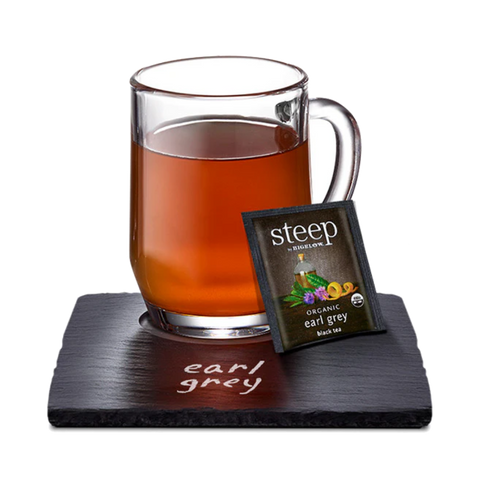 Glass mug of copper-colored Earl Grey with a Steep tea bag on a slate coaster
