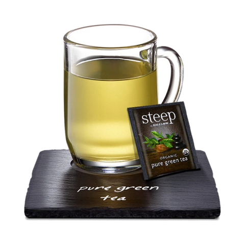 Glass mug of pale green tea with a Steep tea bag on a slate coaster