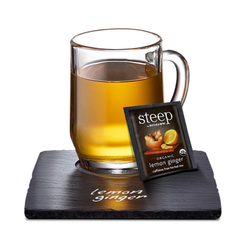 Glass mug of amber lemon ginger tea with a Steep tea bag on a slate coaster