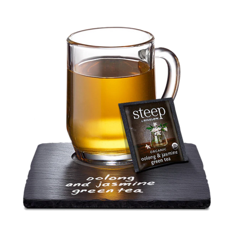 Glass mug of golden oolong jasmine tea with a Steep tea bag on a slate coaster
