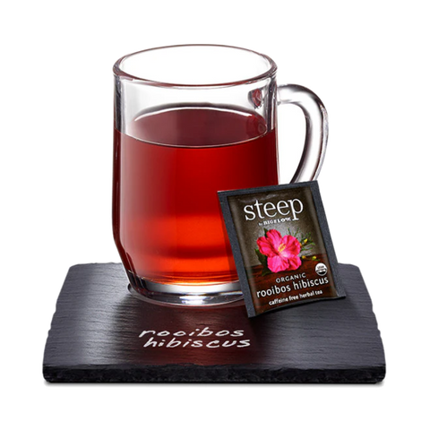 Glass mug of deep red rooibos hibiscus tea with a Steep tea bag on a slate coaster