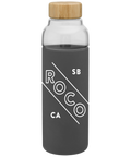 Bali 18 oz glass bottle in a dark gray sleeve printed "RoCo SB CA," with a wood lid